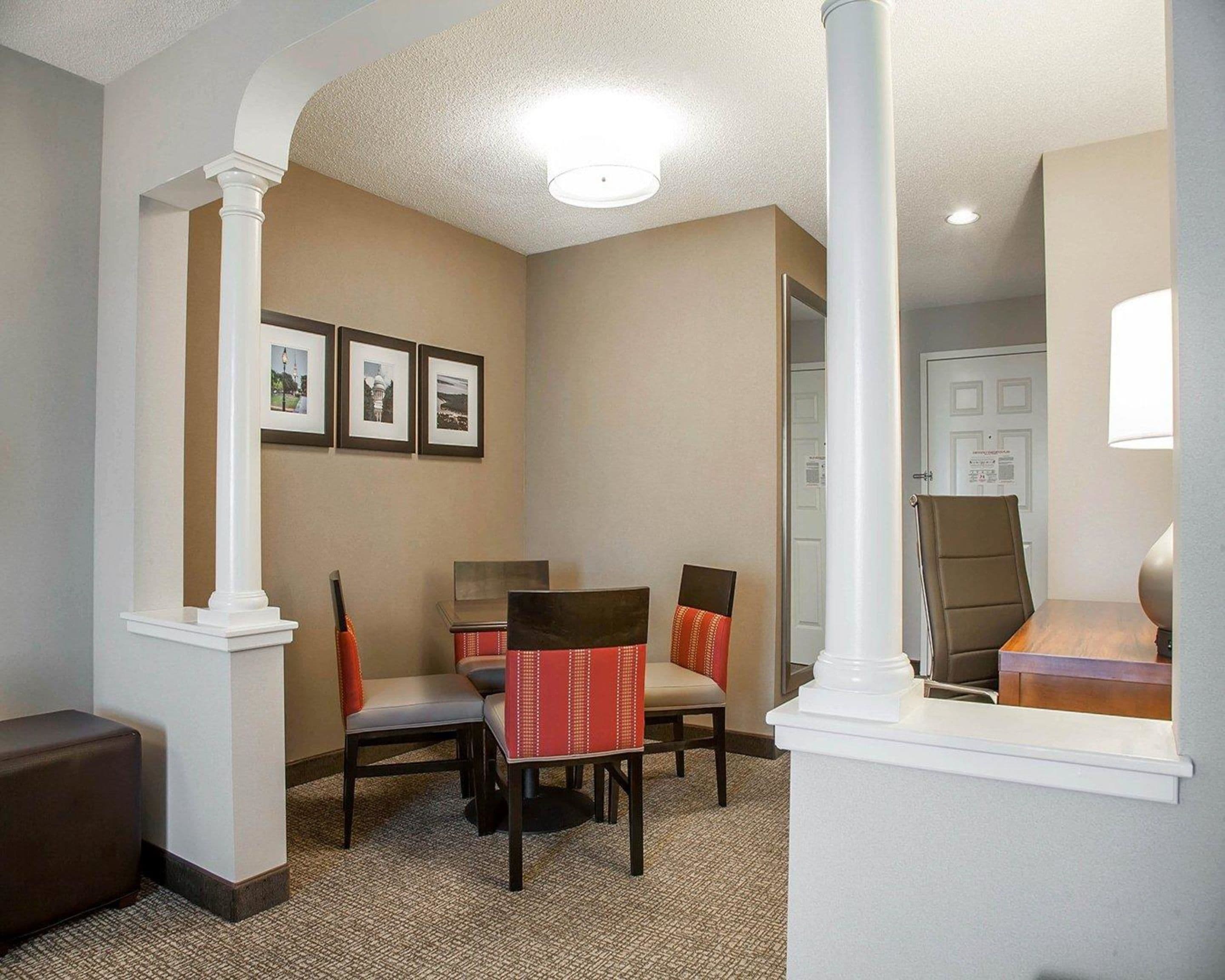 A hotel lobby with a reception desk, two chairs, a sofa, and framed pictures on the wall.