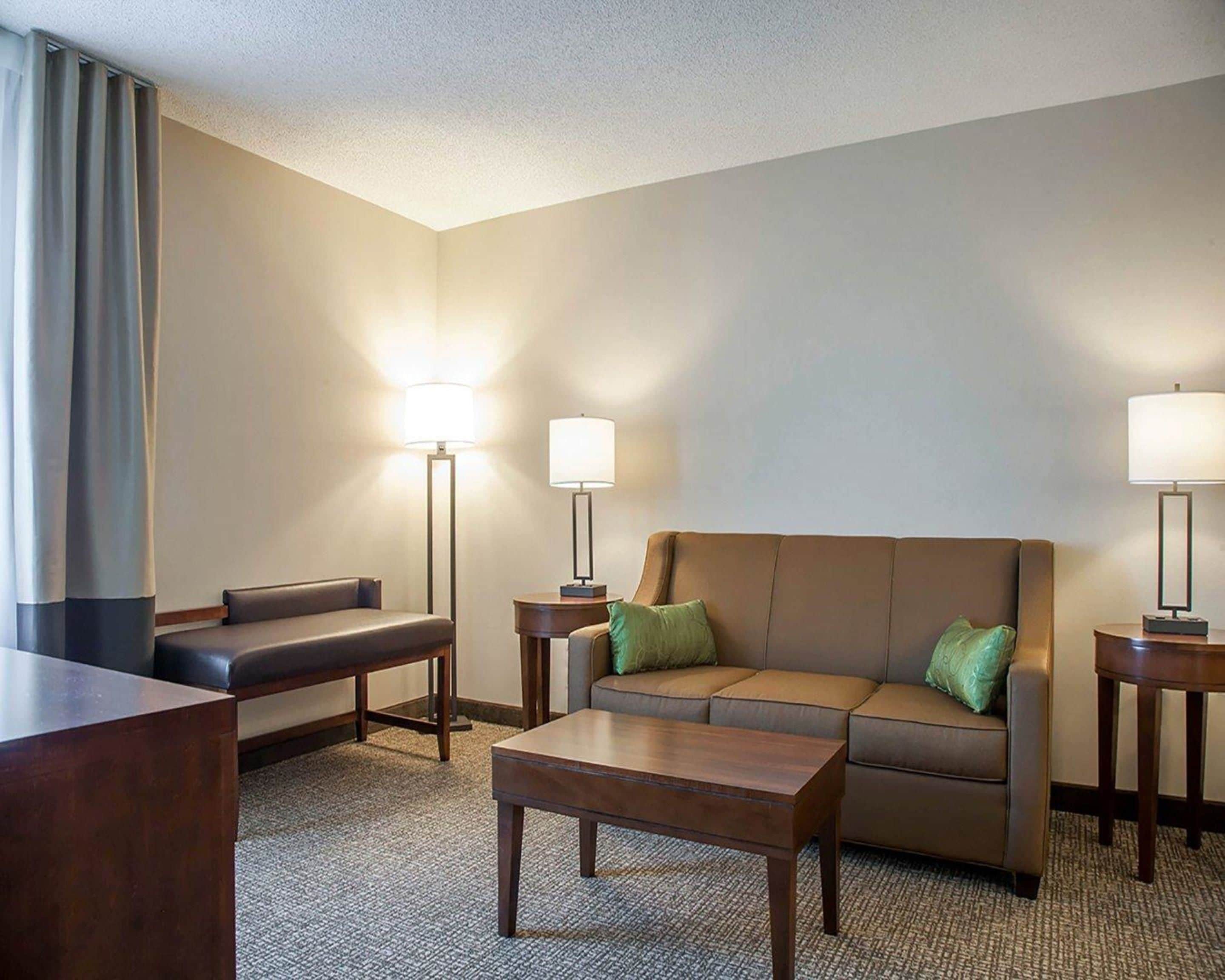Habitación de hotel con sofá, una mesita, dos lámparas y un escritorio.