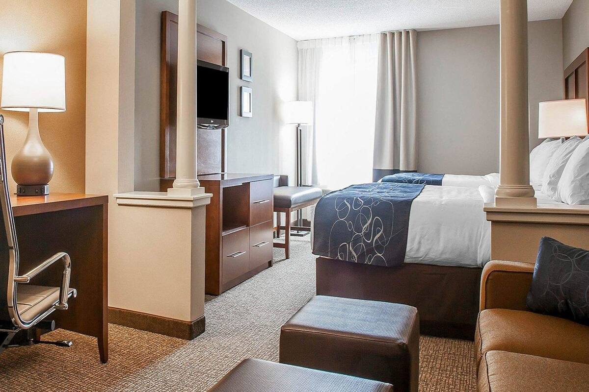 A hotel room with a bed, a desk, a chair, a TV, and a large window with curtains.