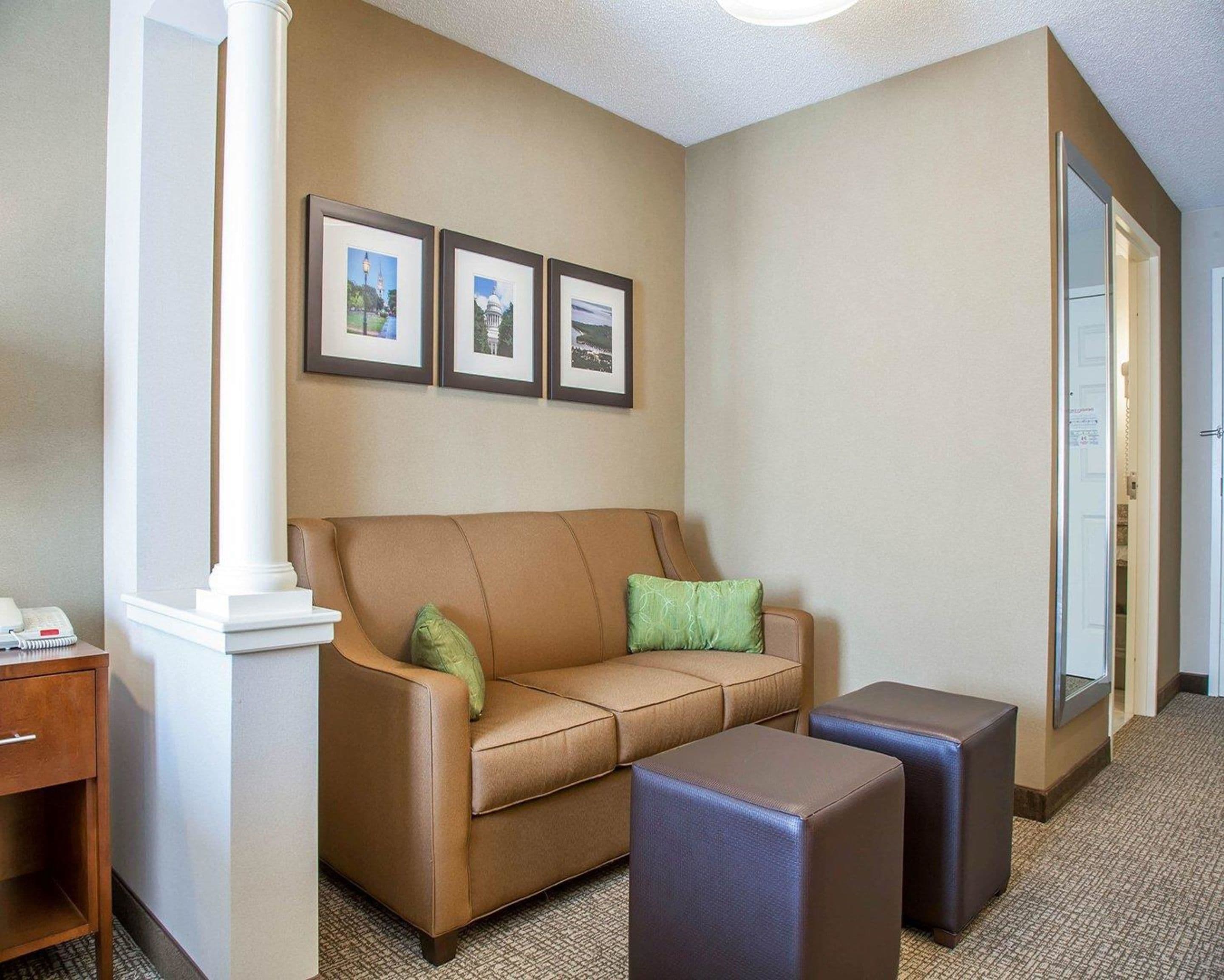Un hall d’hôtel avec un canapé en cuir marron, deux poufs assortis, une table d’appoint en bois avec un téléphone et des tableaux encadrés accrochés au mur.