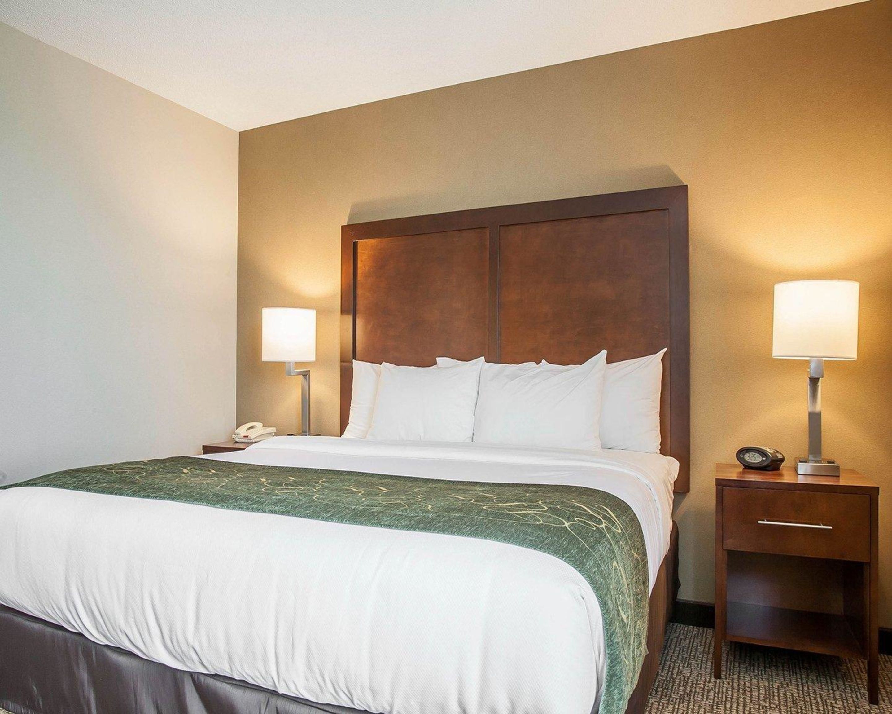A hotel room with a large bed, two bedside tables, a nightstand, and a lamp on each side of the bed.