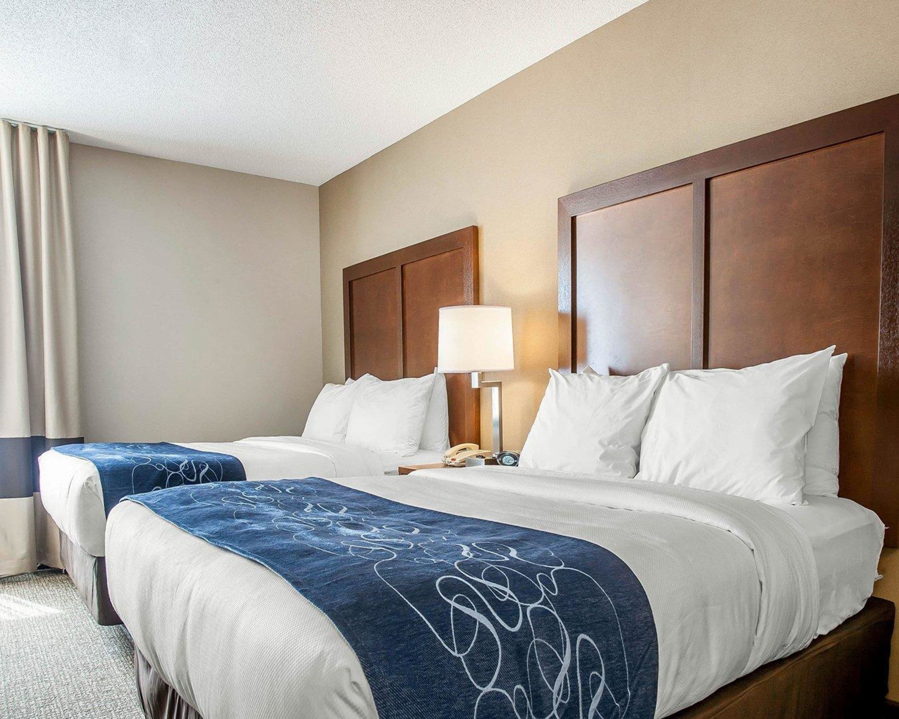A hotel room with two beds, a nightstand with a lamp, and a window with curtains.