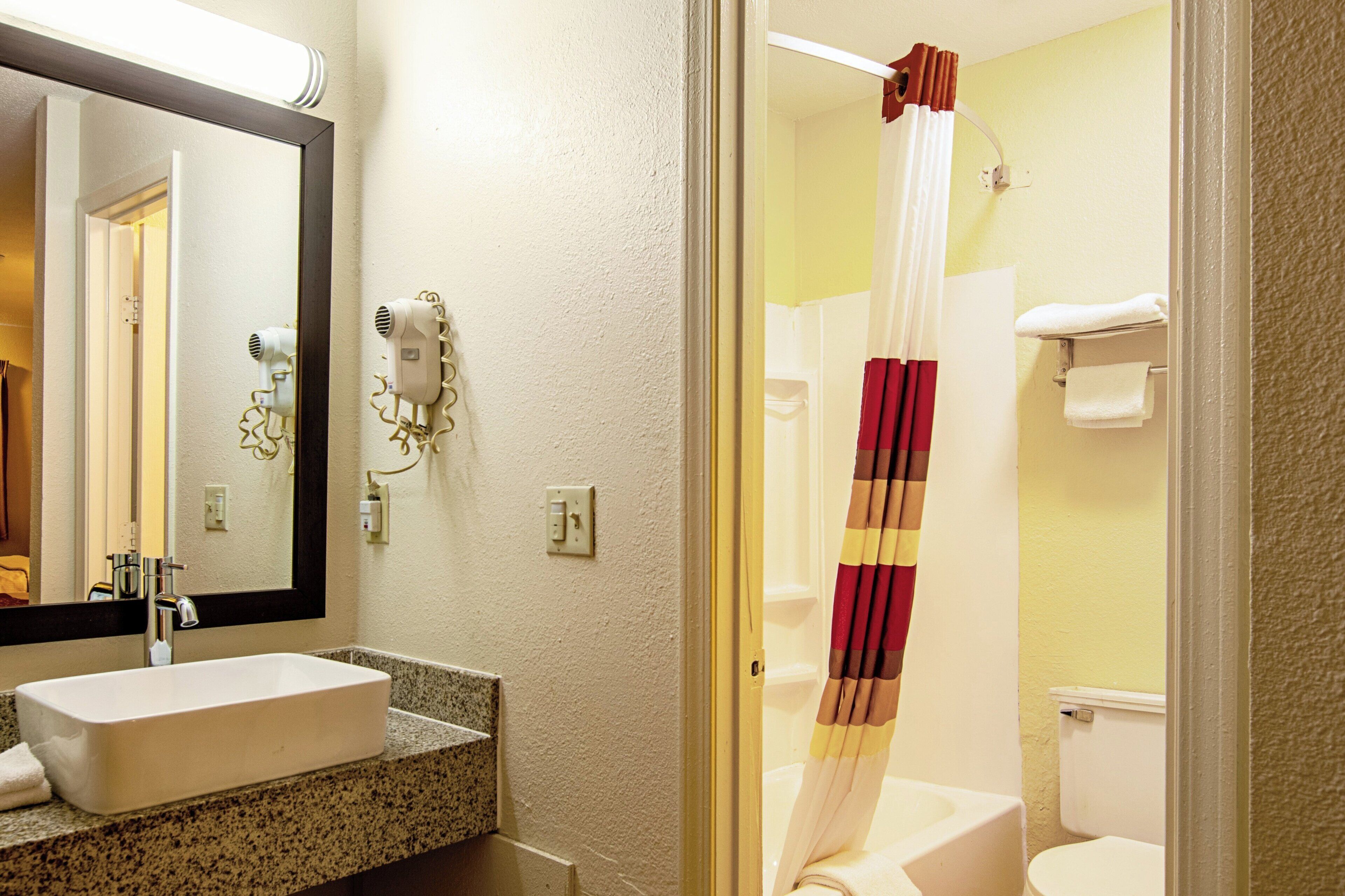 A bathroom with a sink, mirror, hairdryer, and shower curtain.