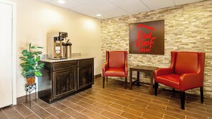A Red Roof Inn lobby with a coffee machine, two leather chairs, a small table, and a potted plant. - Red Roof Inn Scottsburg (Scottsburg)