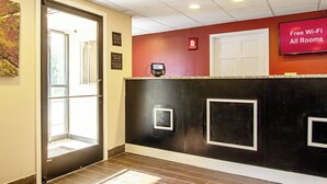 A hotel reception area with a check-in counter, a door, and a sign indicating free Wi-Fi availability. - Red Roof Inn Scottsburg (Scottsburg)