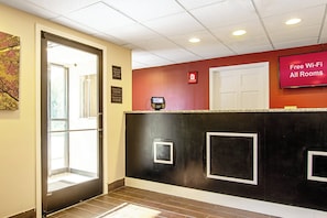 A hotel reception area with a check-in counter, a door, and a sign indicating free Wi-Fi availability. - Red Roof Inn Scottsburg (Scottsburg)