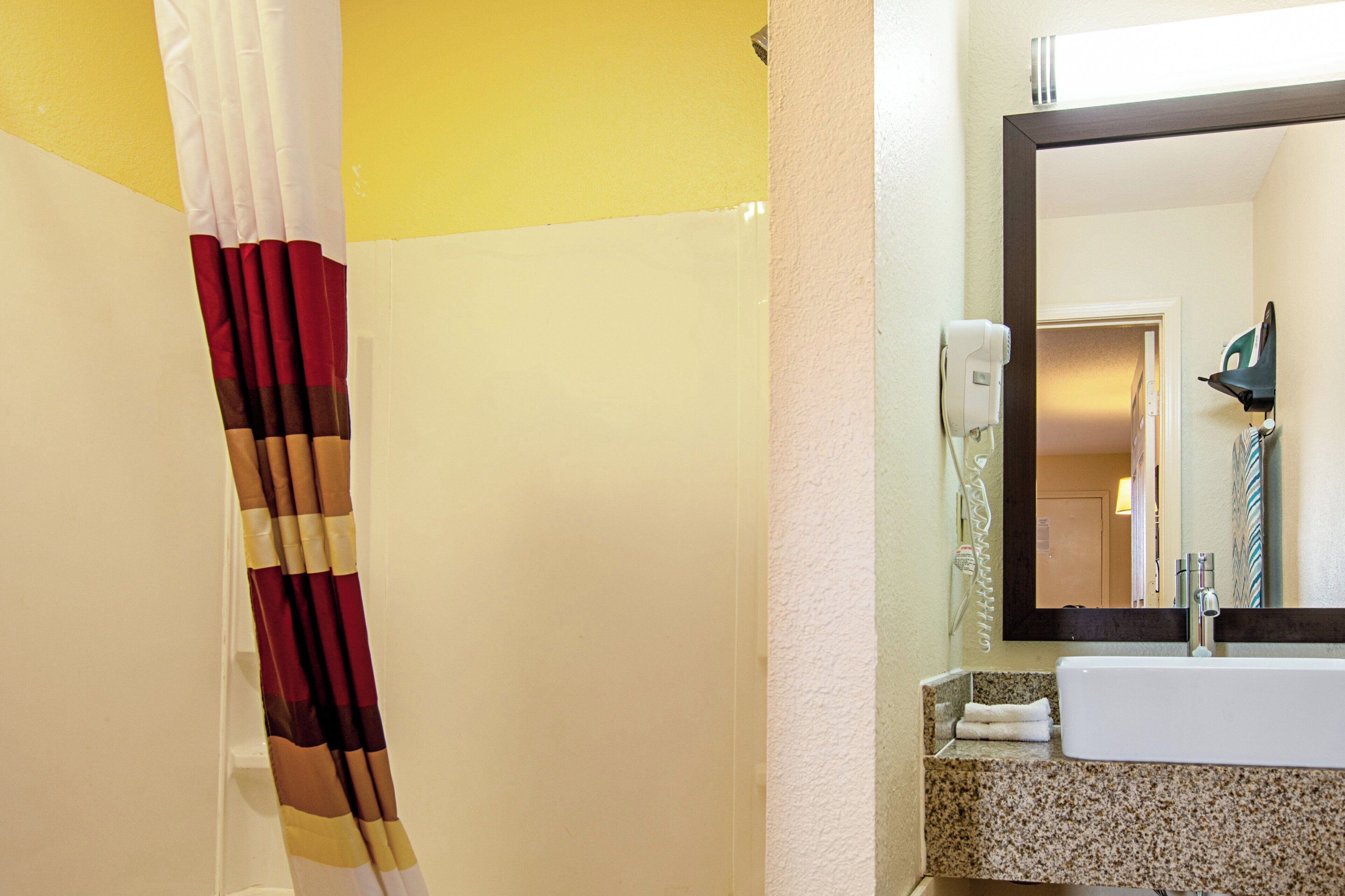 Un baño con cortina de ducha, lavamanos, espejo y secador de pelo en la pared.