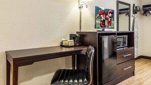 A hotel room with a wooden desk, a black leather chair, a refrigerator, a coffee maker, a framed picture on the wall, and a mirror. - Red Roof Inn Scottsburg (Scottsburg)