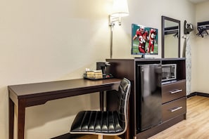 A hotel room with a wooden desk, a black leather chair, a refrigerator, a coffee maker, a framed picture on the wall, and a mirror. - Red Roof Inn Scottsburg (Scottsburg)