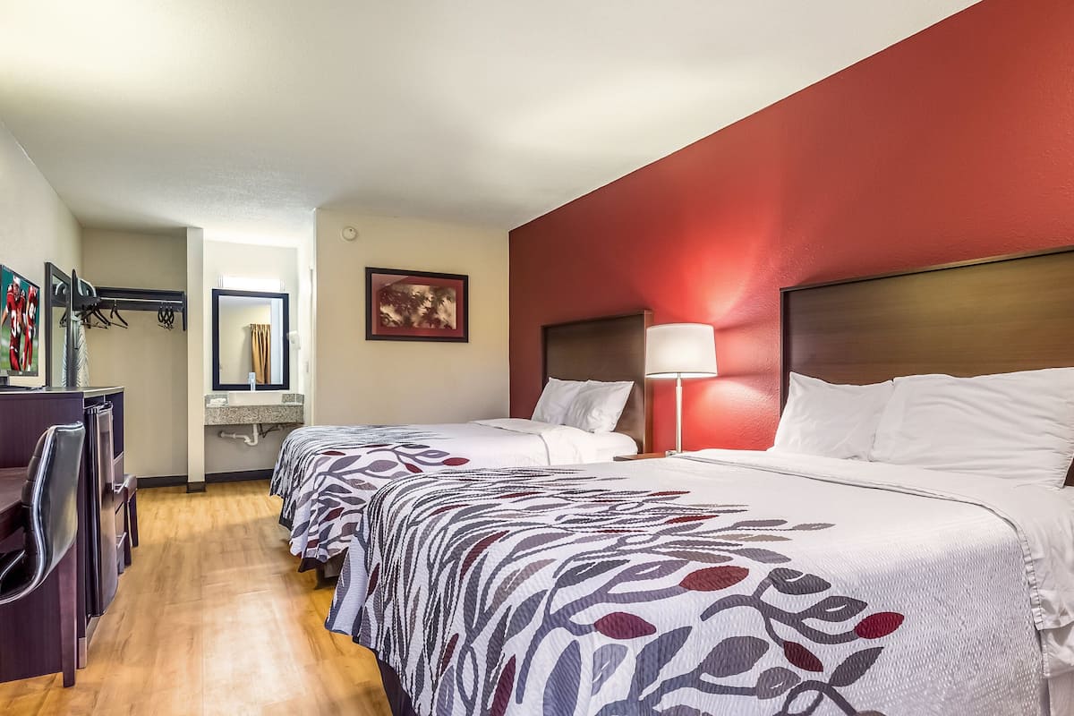 A hotel room with two beds, a desk, and a mirror.