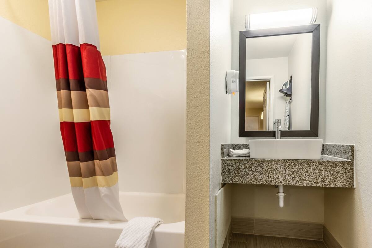 A bathroom with a bathtub, a shower curtain, a sink, and a mirror.