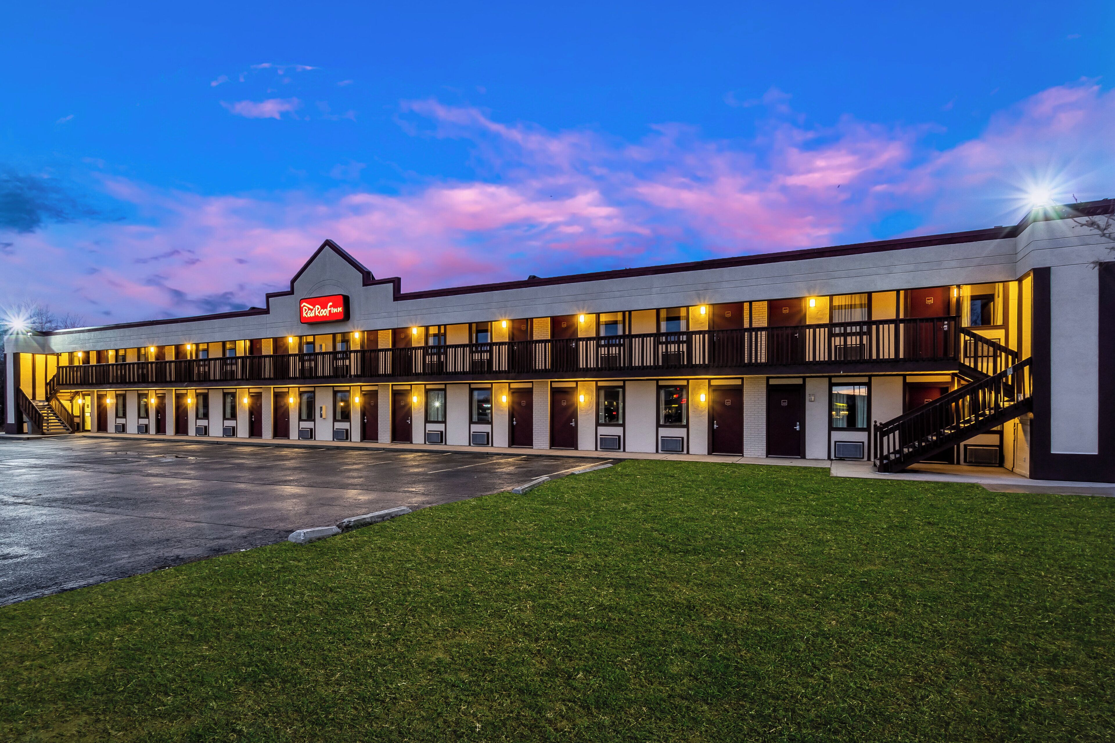 Un hôtel Red Roof Inn avec un bâtiment à deux étages, un espace de stationnement couvert et une pelouse bien entretenue.