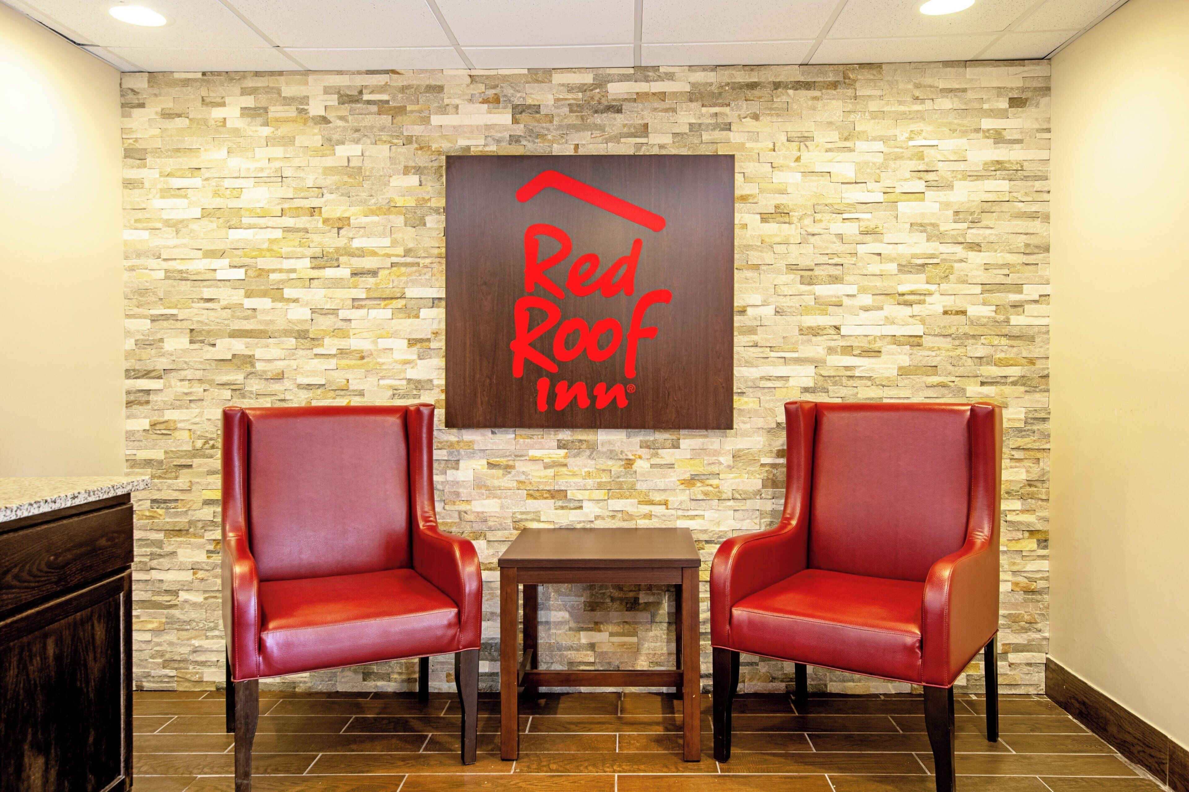 A Red Roof Inn with two red leather chairs and a small table in a lobby area.