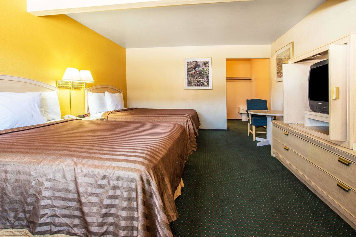 Une chambre d’hôtel avec deux lits, un bureau, une chaise, une télévision et une armoire.