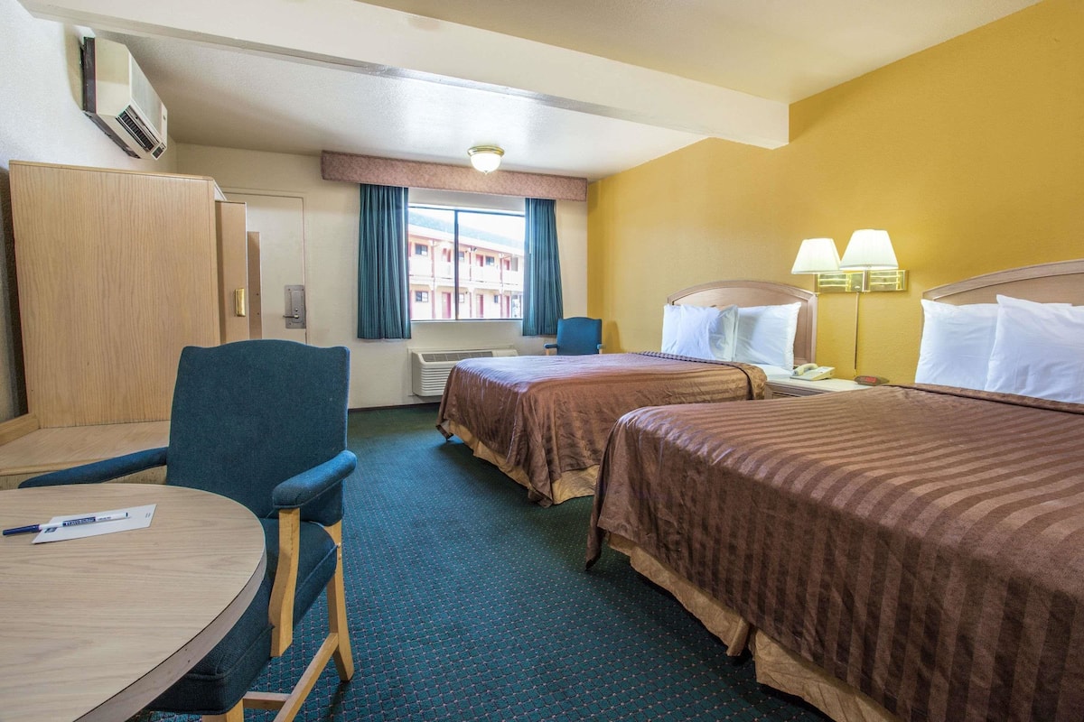 Une chambre d’hôtel avec deux lits, un bureau, une chaise, une fenêtre avec des rideaux, une lampe et un appareil de climatisation.