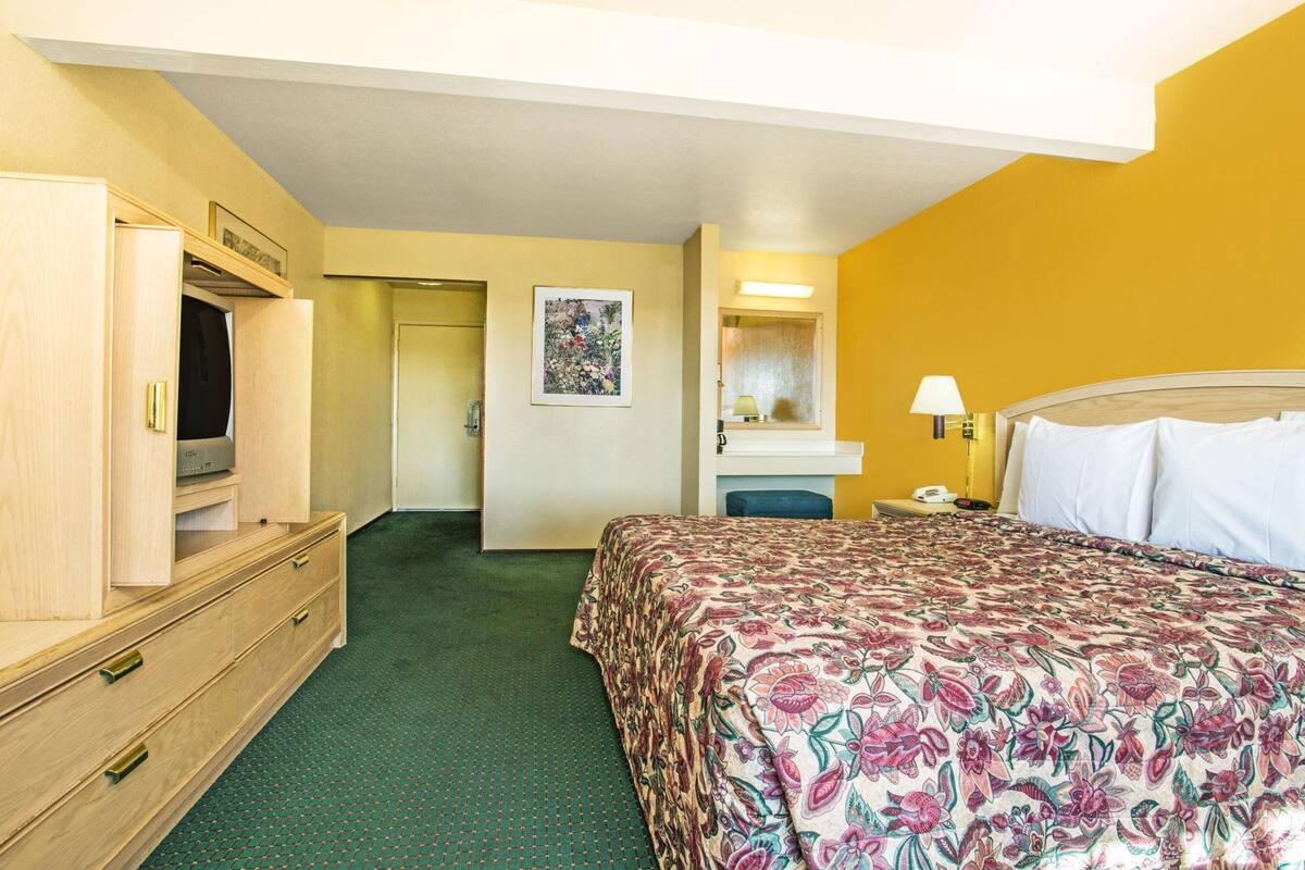 Une chambre d’hôtel comprenant un lit, une commode, une télévision, un miroir et une porte donnant sur une autre pièce.