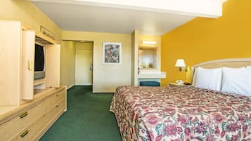 A hotel room with a bed, a dresser, a mirror, and a door leading to another room.