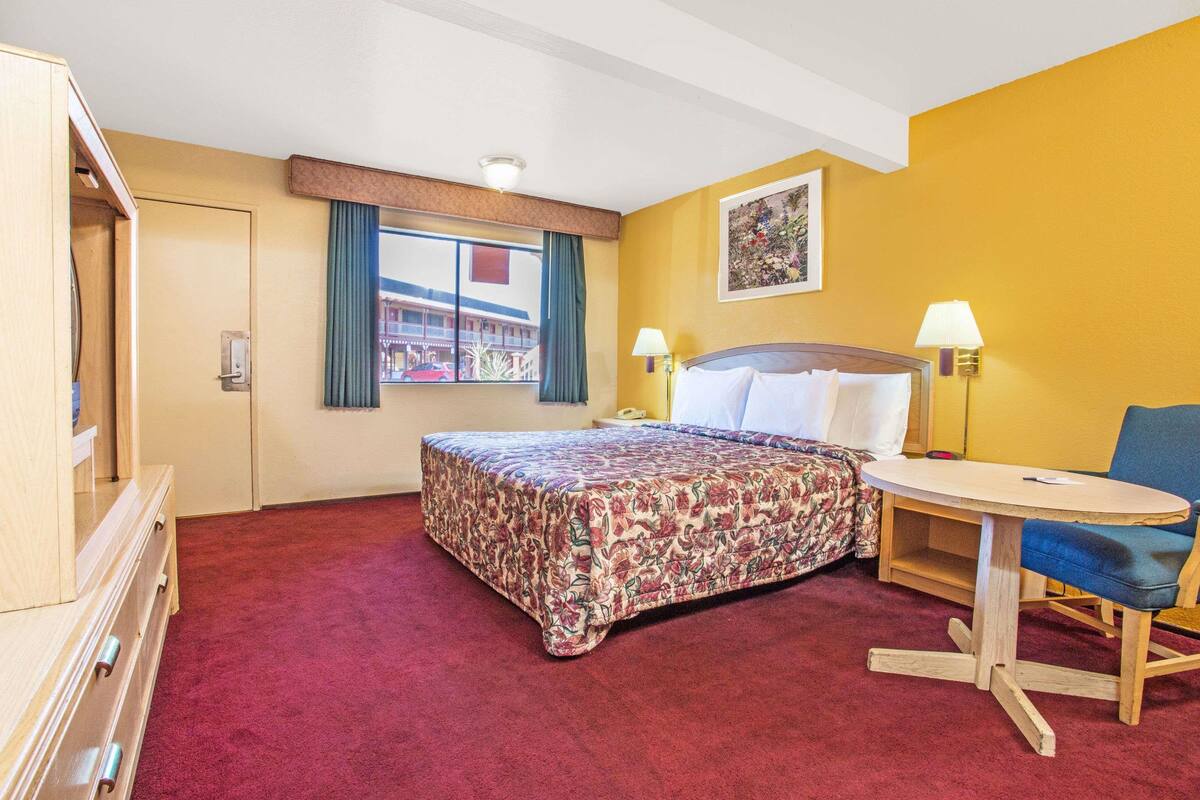 Une chambre d’hôtel avec un lit, un bureau, une chaise, une commode et une fenêtre avec des rideaux.