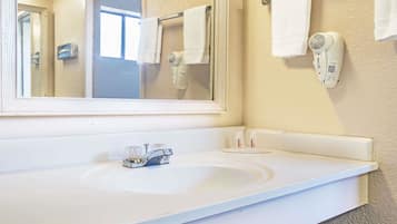 Un bagno con un lavandino bianco, uno specchio e un asciugacapelli fissato alla parete.