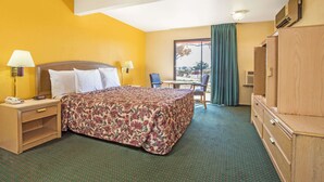 Una habitación de hotel con cama, escritorio, silla, armario y ventana con cortinas.