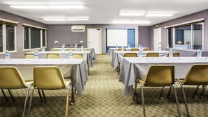 Un salón de conferencias con mesas, sillas y una pantalla de proyector.