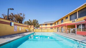 Una piscina con agua cristalina azul, rodeada por un edificio amarillo con toldo rojo.