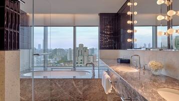 A modern bathroom with a large window, a bathtub, two sinks, and a mirror with lights.
