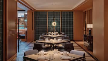 A hotel dining area with multiple tables, chairs, and a central decorative light fixture.