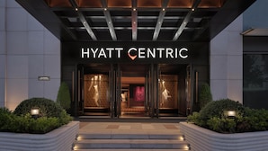 The entrance of the Hyatt Centric hotel with a modern design, featuring a prominent sign, steps leading up to the entrance, and well-maintained landscaping.