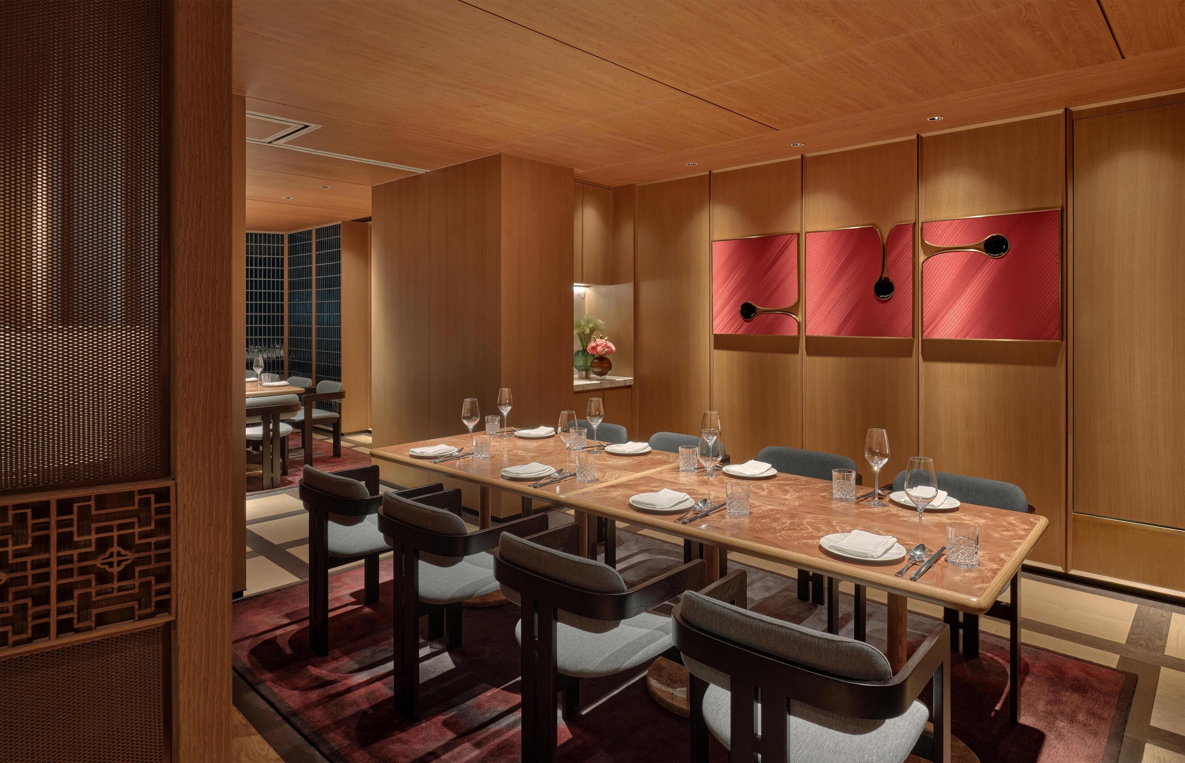 A hotel dining area with a long table set for six, surrounded by chairs, and a decorative wall with three red panels.