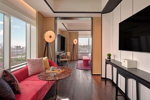 Una habitación de hotel moderna con un ventanal grande, un sofá, una mesita, un televisor y un escritorio.