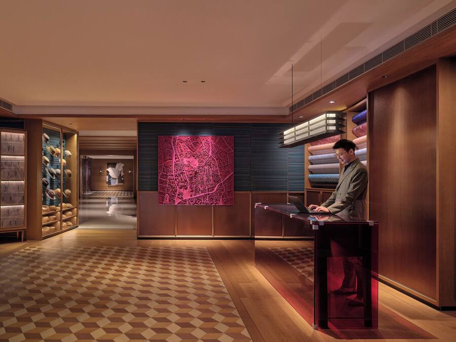 A modern hotel lobby with a check-in counter, a large map mural, and plush seating areas.