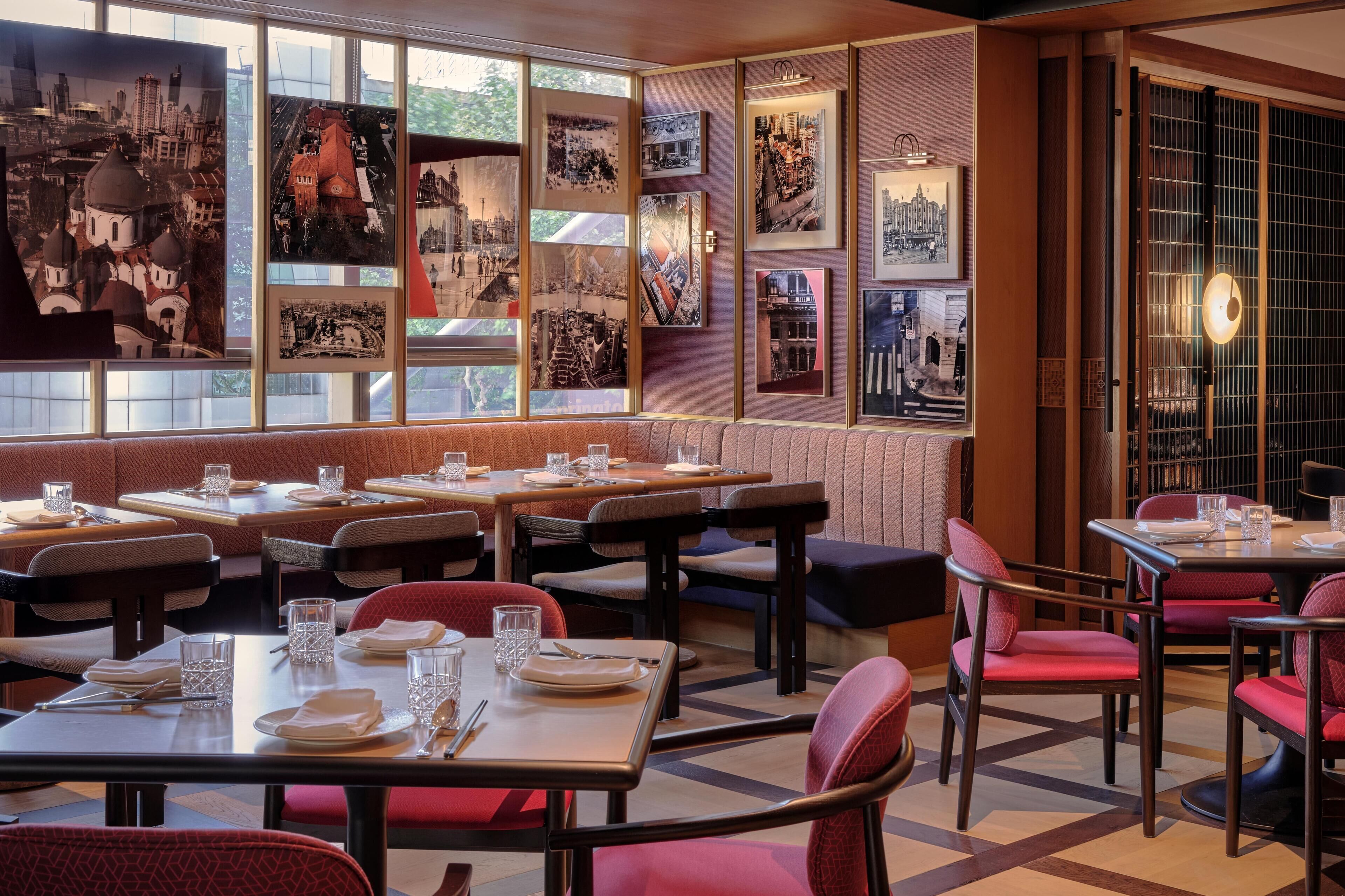 A restaurant with multiple tables and booths, framed pictures on the walls, and a view through large windows.
