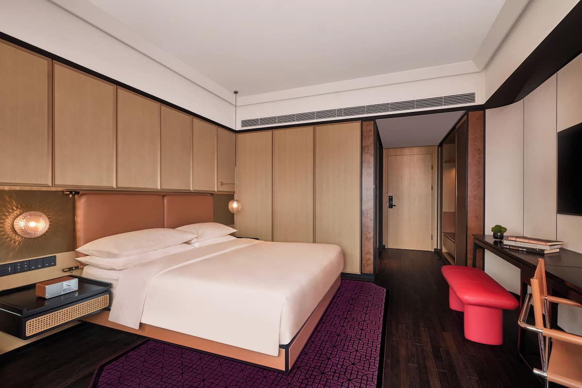 A modern hotel room with a large bed, a desk, a red bench, and a TV.