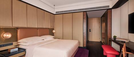 A modern hotel room with a large bed, a desk, a red bench, and a TV.