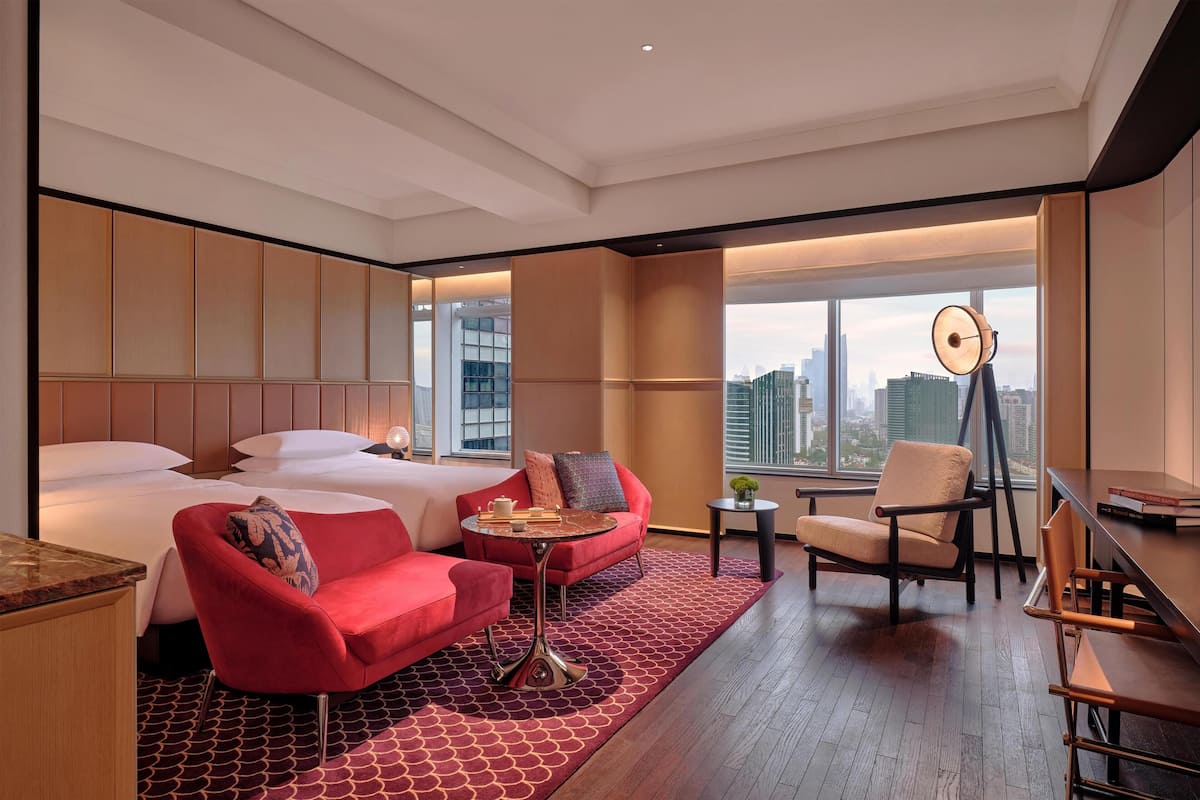A hotel room with a bed, red armchair, round coffee table, and a desk with a chair.