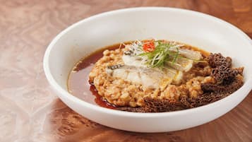 A bowl of food with a fish, sauce, and garnishes on a wooden table.
