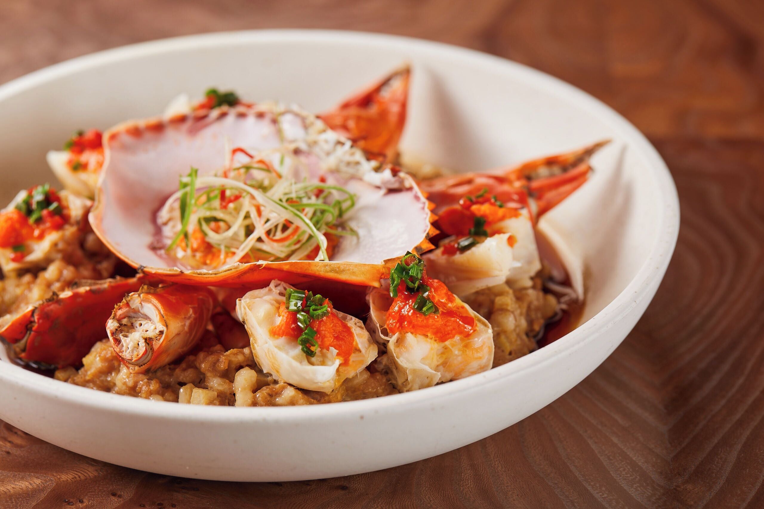 A bowl of seafood chowder with crab legs and a scallop on top.