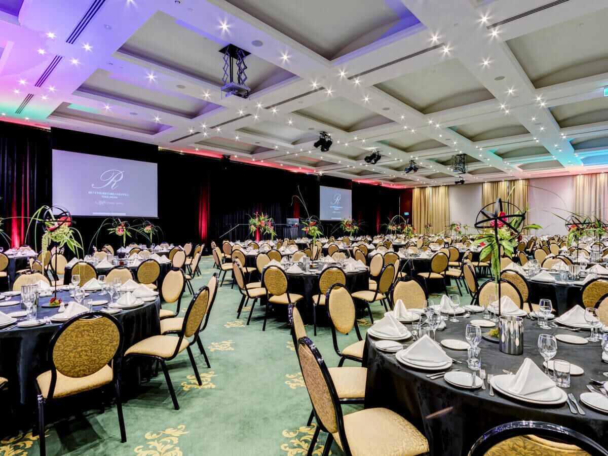 A banquet hall with round tables, chairs, and a stage with a screen.