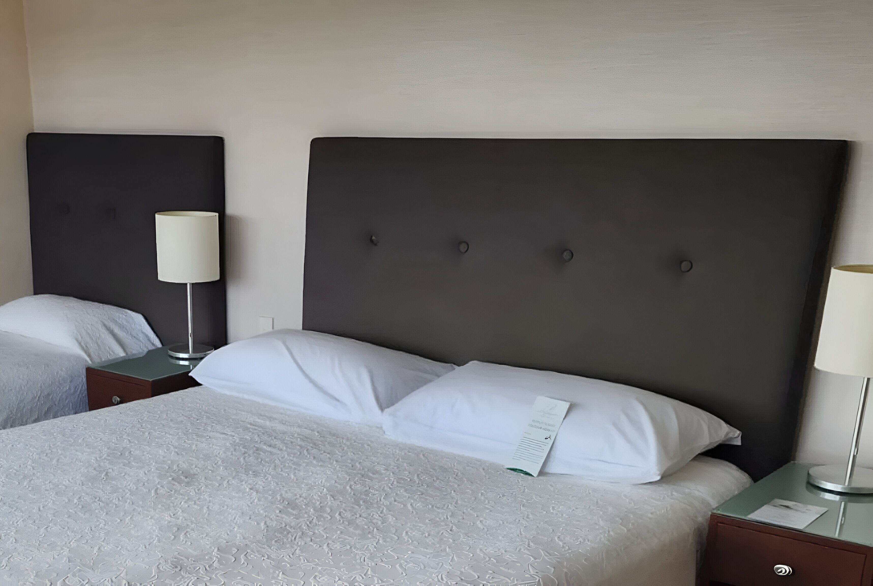 A hotel room with a large bed, two bedside tables, and a dark headboard.