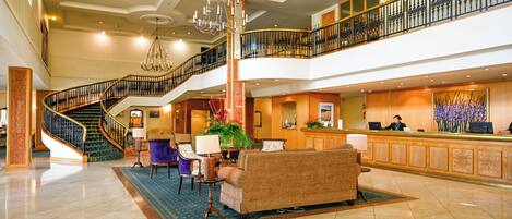 A spacious lobby with a grand staircase, a reception desk, and comfortable seating areas.