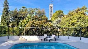 A swimming pool with two lounge chairs, surrounded by a metal fence and trees.