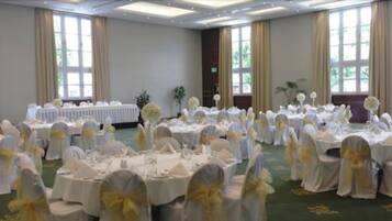 Un salón de banquetes con mesas redondas cubiertas con manteles blancos y sillas adornadas con cintas amarillas, dispuesto para un evento formal.