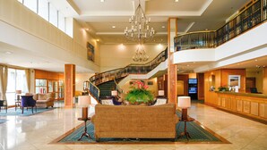 A spacious lobby with a grand staircase, a reception desk, and a chandelier.