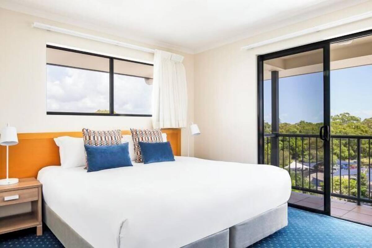 Une chambre d’hôtel avec un grand lit, une table de chevet, une fenêtre et un balcon avec vue.