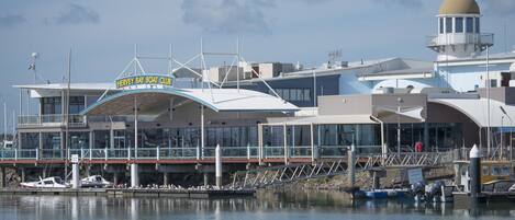 Un port de plaisance avec des bateaux amarrés, un hangar à bateaux et un bâtiment surmonté d’un dôme et portant une enseigne indiquant « HERVEY BAY BOAT CLUB ».