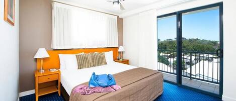 A hotel room with a bed, two bedside tables, a ceiling fan, a large window with a view, and a balcony.