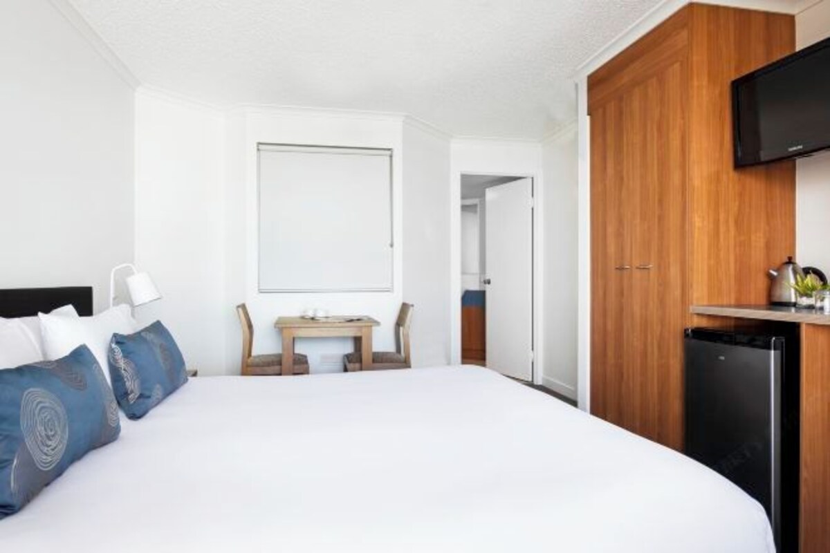 Habitación de hotel con cama, escritorio, televisor y armario.