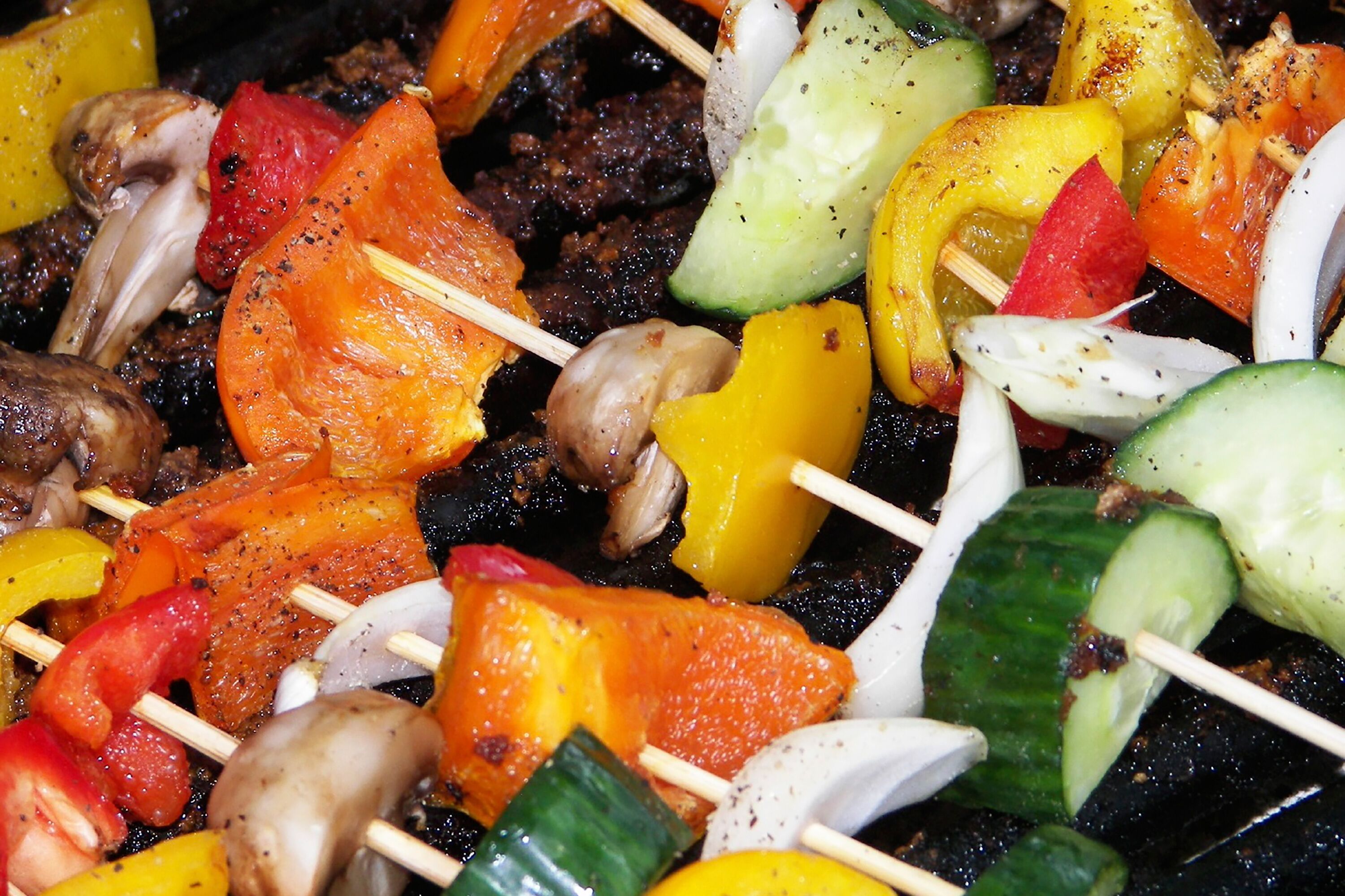 A close-up of colorful vegetable and meat skewers on a grill.