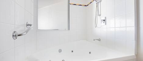 A modern bathroom with a large white bathtub, a handheld showerhead, and a wall-mounted faucet.